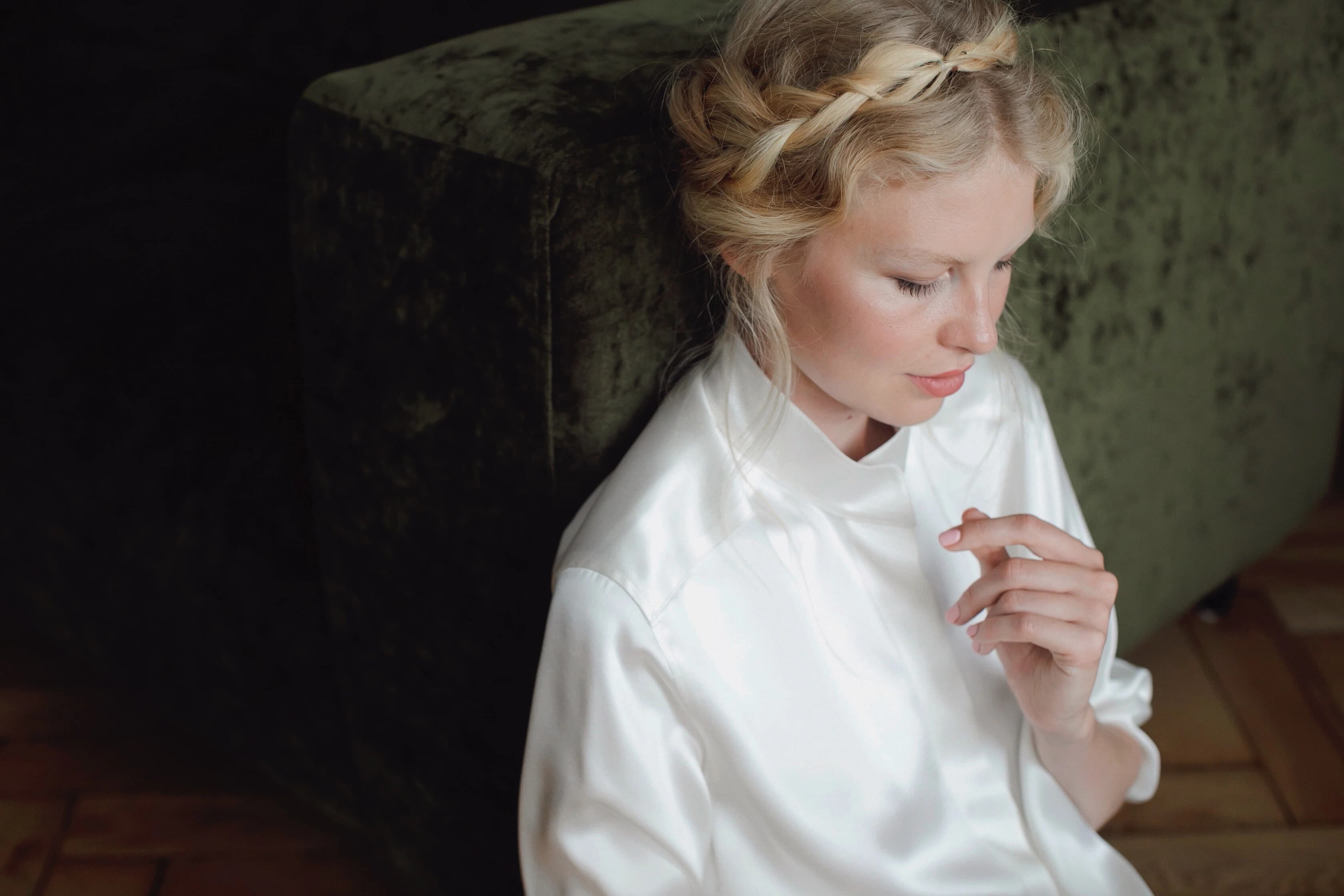 A woman seated on the floor in a white silk lounge shirt, looking down.